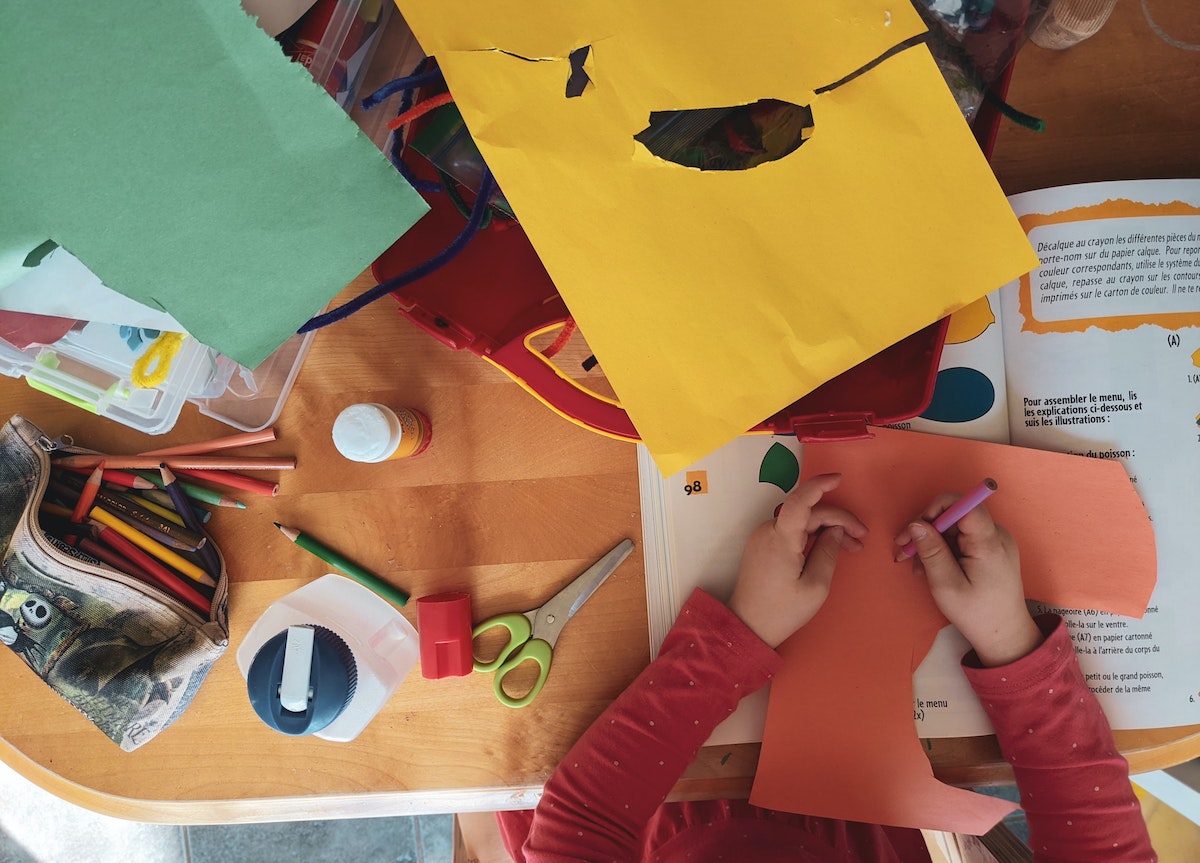 A child at a wooden table surrounded by colorful arts and crafts